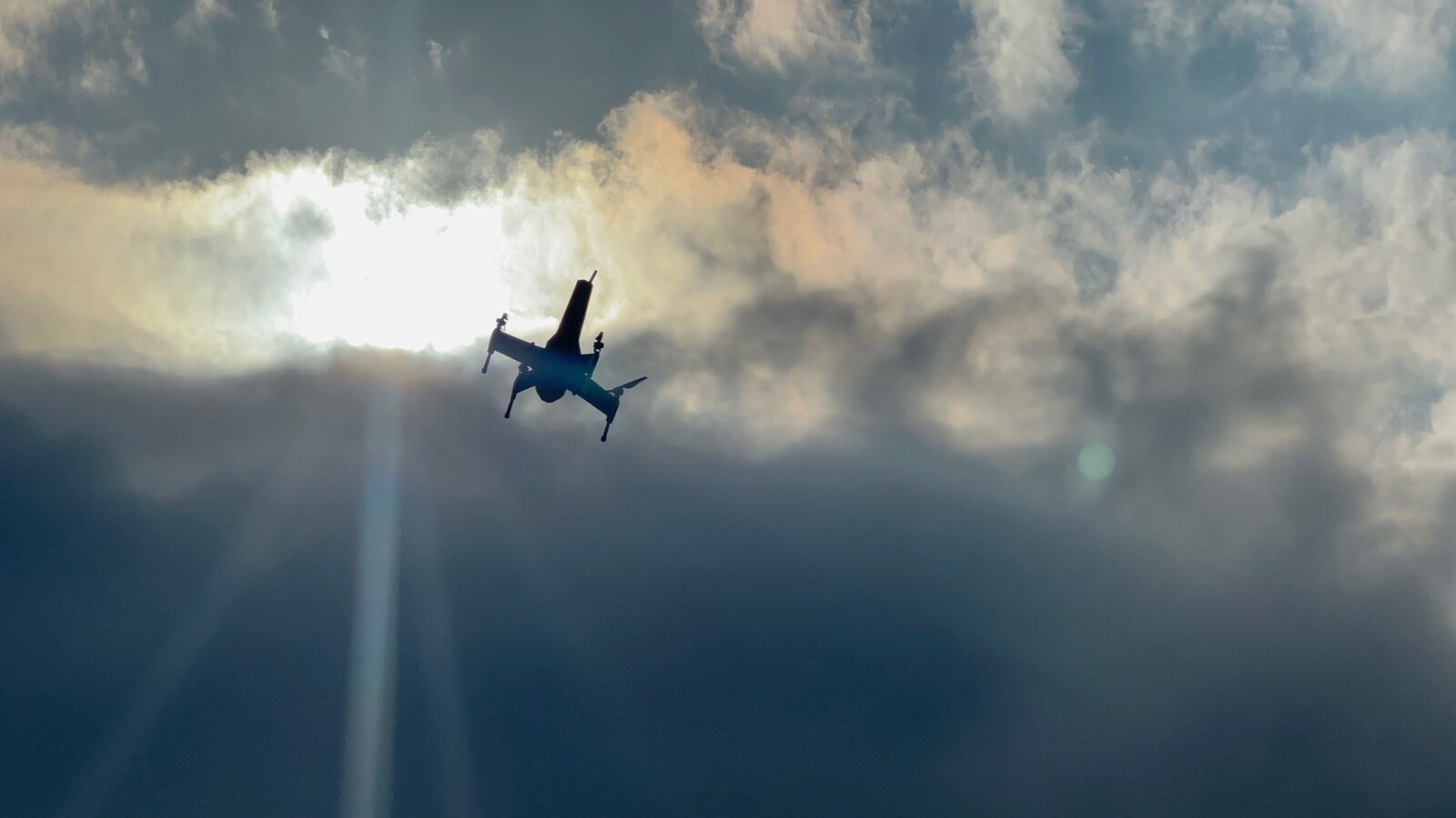 Orbital composite drone in flight against sun and clouds